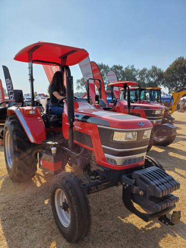 Girl with brown curly hair, wearing blue jeans, sitting confidently on a large red tractor